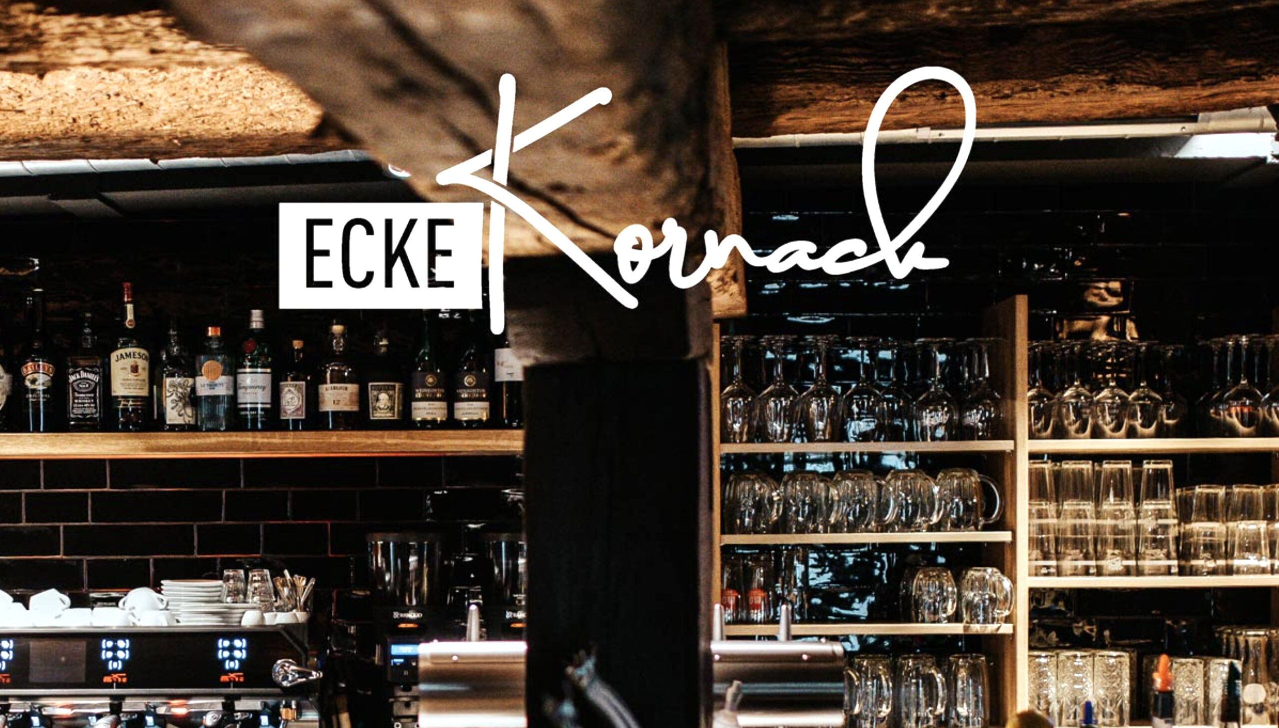 Auf dem Bild ist die Rückwand einer Bar zu erkennen. Links unten ist eine Kaffeemaschine. Recht stehen die Gläser auf den Regalen. Das Licht ist schummrig, das Ambiente gemütlich. Über dem Bild liegt der Schriftzug Ecke Kornack.